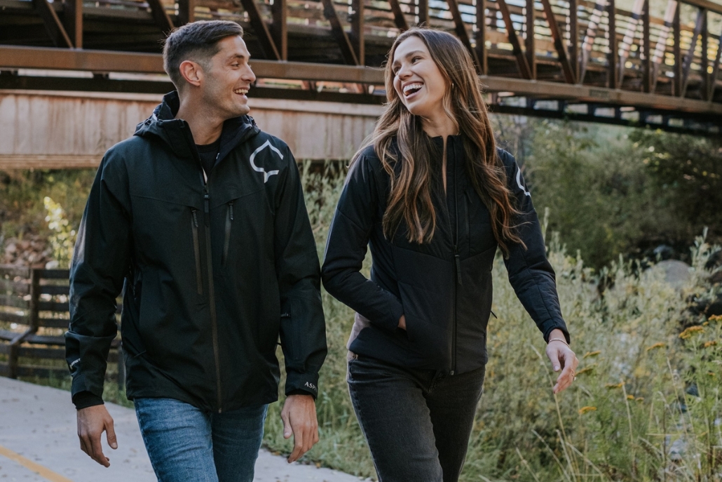 A couple walks together on a path, wearing stylish light jackets and layers, reflecting the Aspen fashion trend during Autumn.