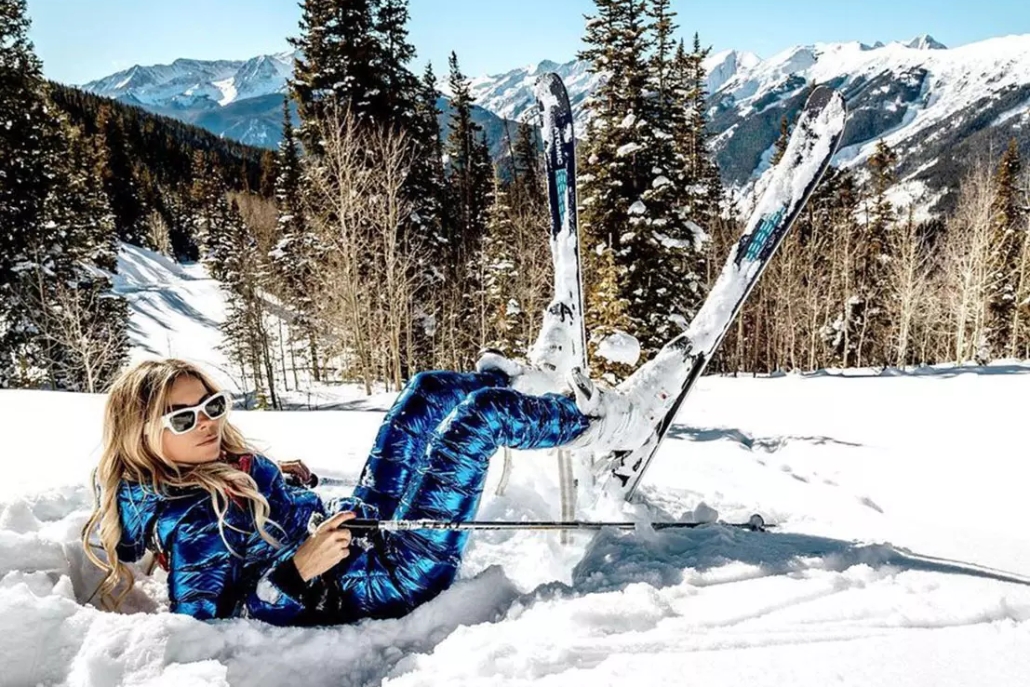 A woman dressed in blue ski attire lies on the snow enjoying the spirit of winter in Aspen.