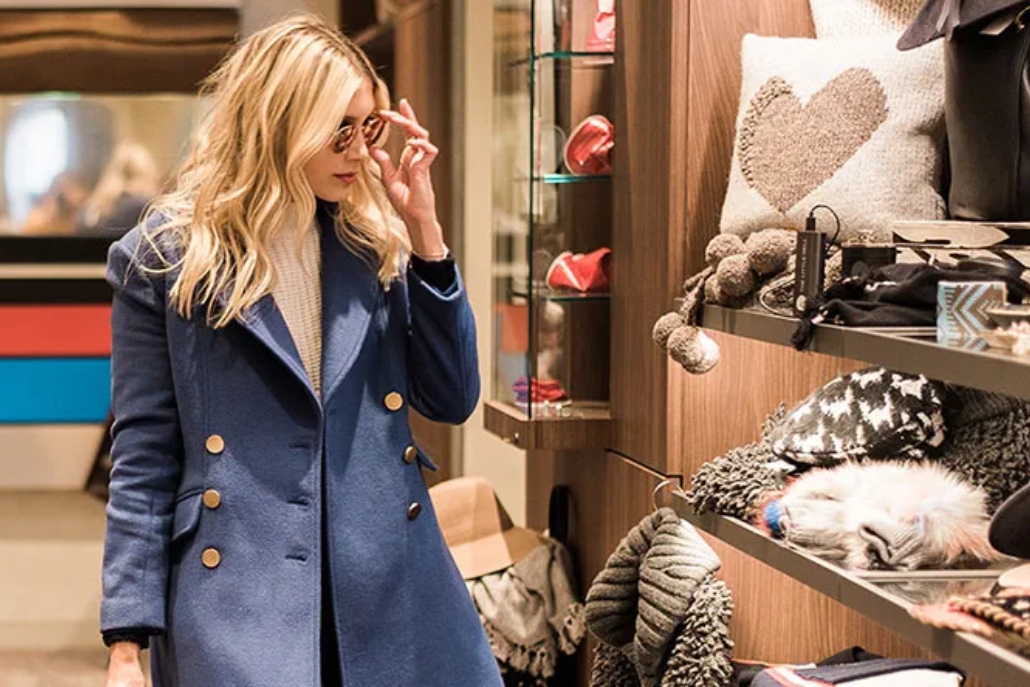 A woman wearing a blue coat and glasses looking for warm scarves and accessories in an Aspen.