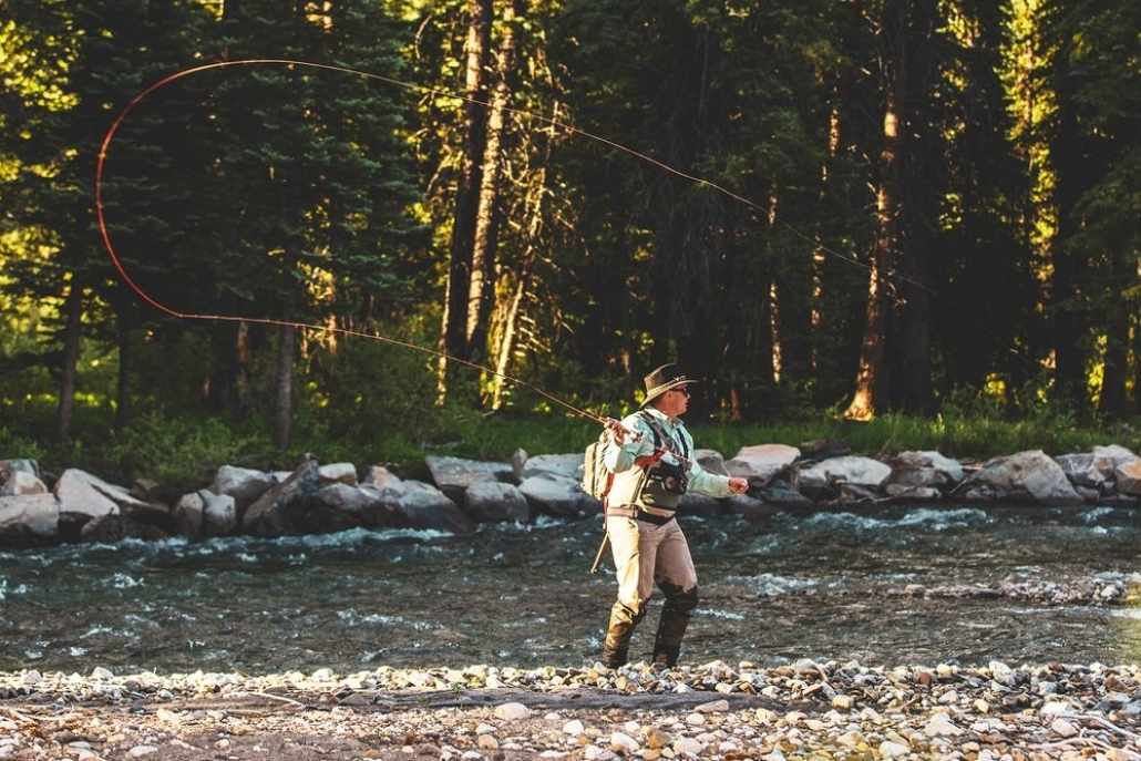 A man fly fishing in a serene river, surrounded by nature's beauty.