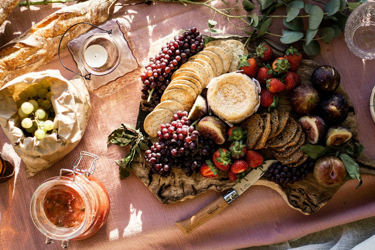 Flat-lay of summer picnic set with fruit, cheese, sausage, bagels over linen table cover, top view