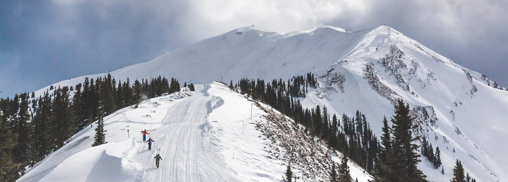 A skier gracefully descends a snowy slope in Highland Bowl Aspen, surrounded by majestic mountains.