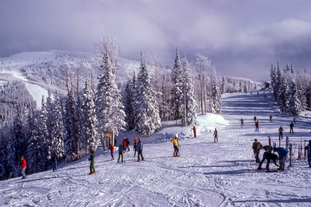 A group of skiers enjoying the slopes at Buttermilk Ski Resort in Aspen, Colorado, surrounded by snowy mountains.