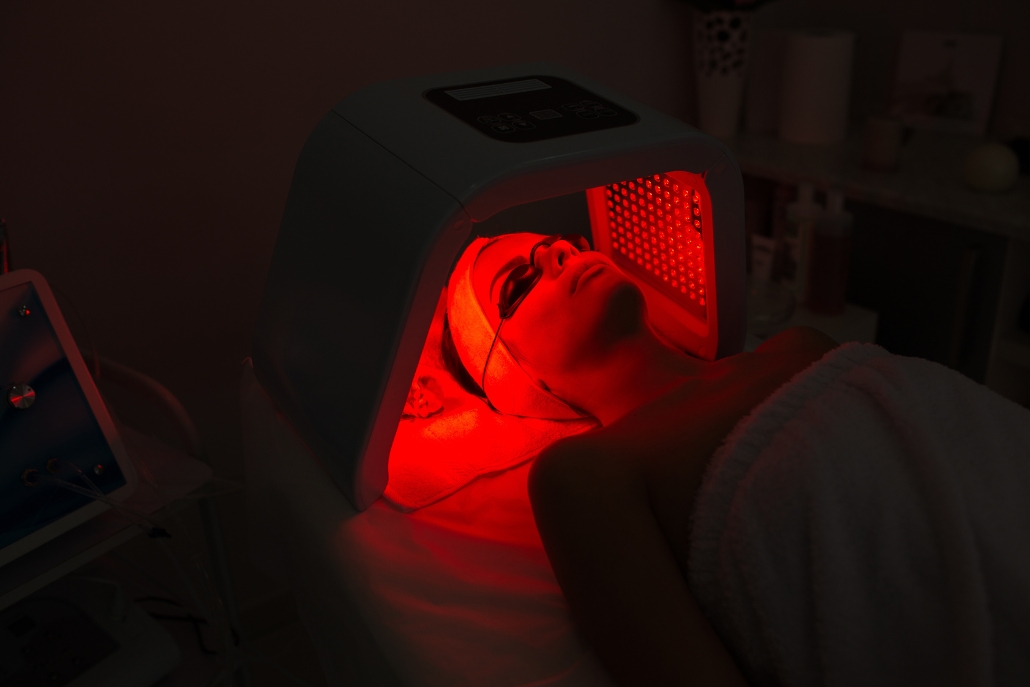 A woman relaxes in bed with a red light illuminating her face at The Dior Spa At The Little Nell in Aspen.