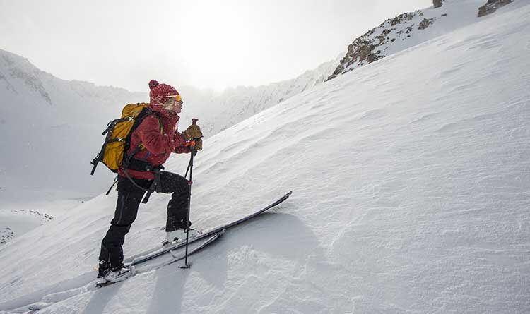 A skier navigating through fresh snow, showcasing the beauty of Aspen Expeditions Skinning in a winter landscape.