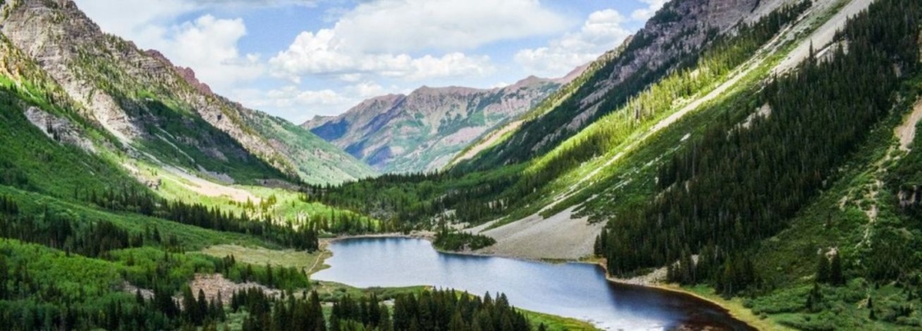 A serene mountain lake framed by lush green trees, showcasing Aspen in August's natural beauty.