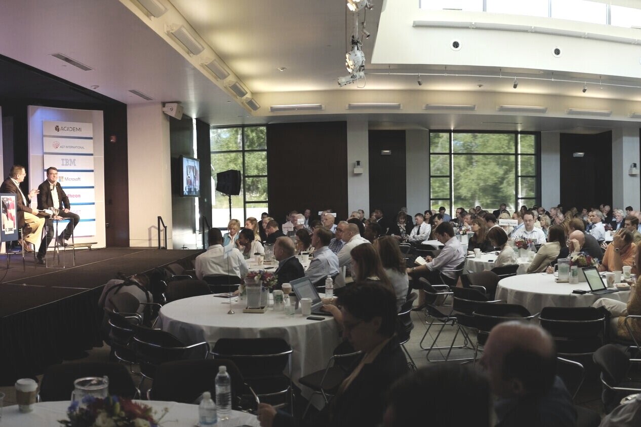 A spacious room filled with attendees seated at tables during meeting at Aspen Luxury Concierge.