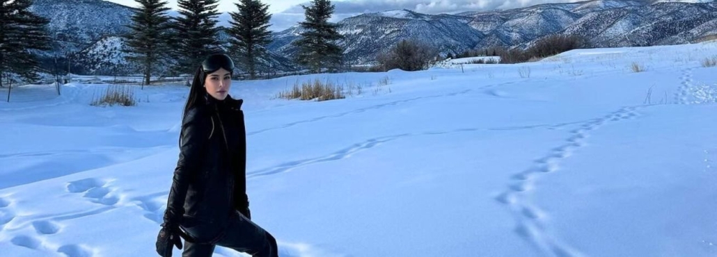 A woman in a black jacket stands on a snowy landscape, showcasing winter fashion.