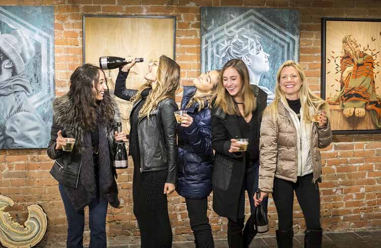 A group of women enjoying their Aspen Girls Trip, standing together in front of vibrant paintings.