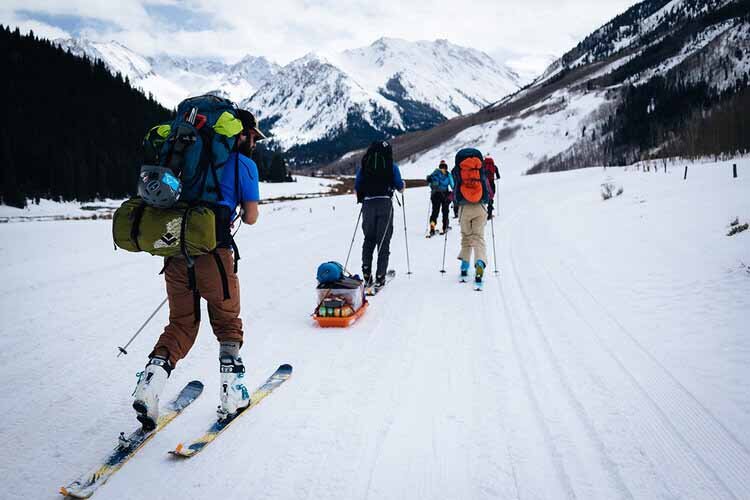 Skiers with backpacks gather for the Aspen Hut Trip, surrounded by a picturesque winter scenery.