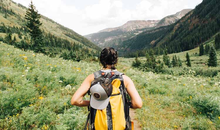 A woman with a backpack strolls through a vibrant meadow, enjoying the beauty of Aspen Hiking.