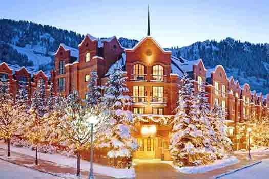 A majestic Aspen Five Star Hotel set against a backdrop of snow-covered trees, beautifully lit for a winter ambiance.