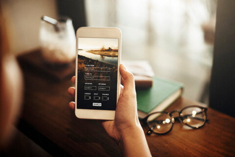 A woman using a smartphone displaying a travel app for Aspen accommodation options.