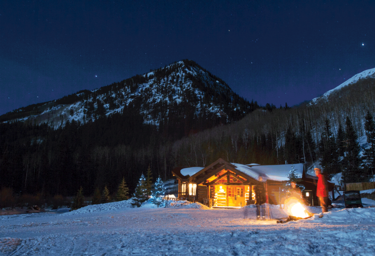 A cozy cabin in the mountains at night, illuminated by a warm fire at Aspen Pine Creek Cook House, perfect for aspen winter experiences.