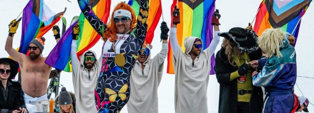 A diverse group of individuals proudly holding rainbow flags at Aspen Gay Ski Week.