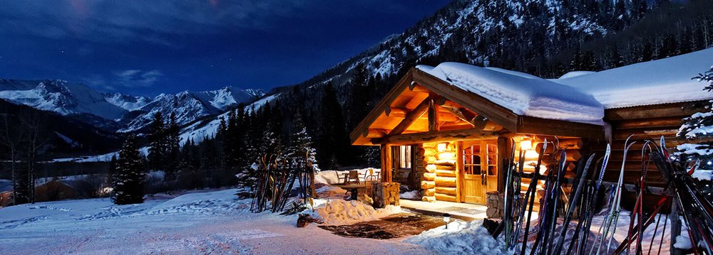 A serene mountain cabin surrounded by snow, glowing softly in the night atmosphere.