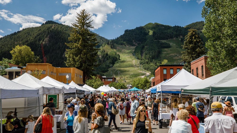 A bustling outdoor market in the mountains, showcasing local goods and a vibrant crowd. One of the best things to do in Aspen in the summer