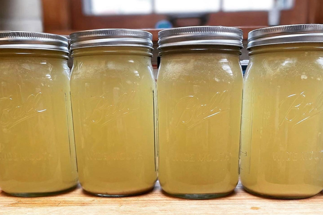 Five jars filled with  bone broths arranged neatly on a countertop surface.