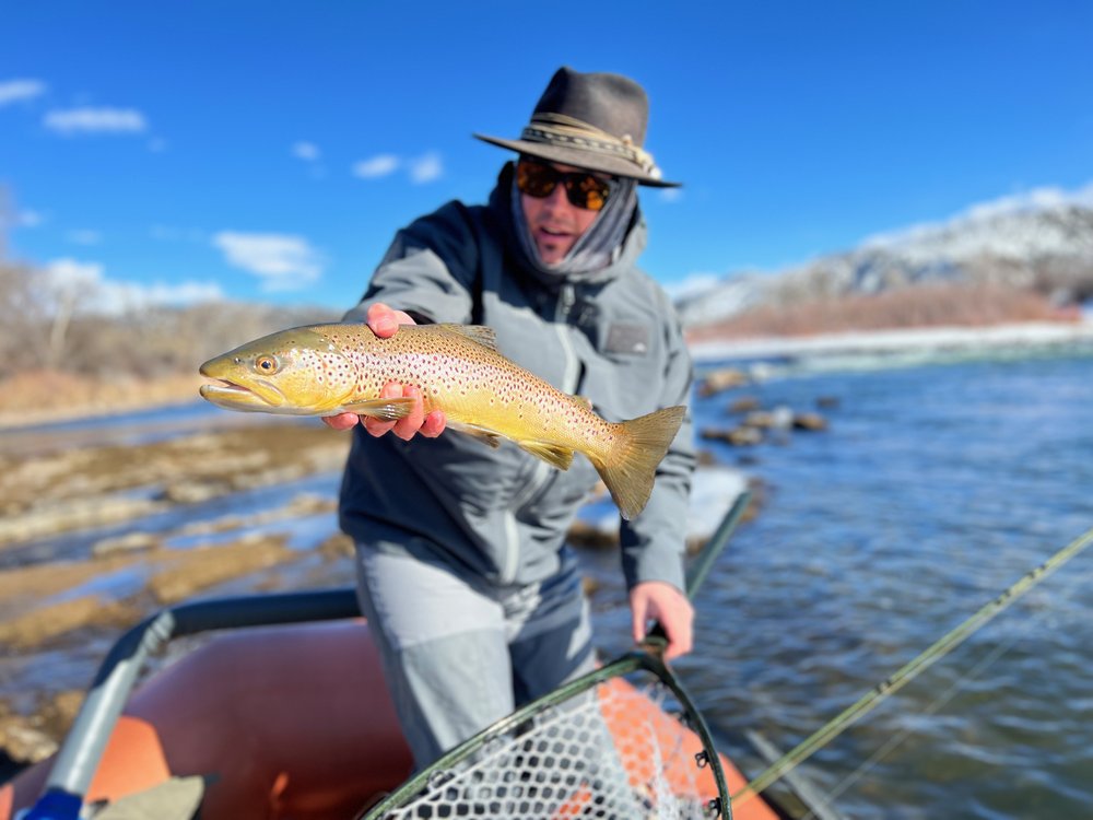 A man with sunglasses and a hat holds a fish, representing his experience in Aspen Fly Fishing.