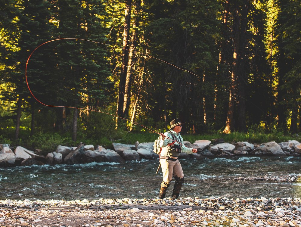 A man fly fishing in a serene river, surrounded by nature's beauty.