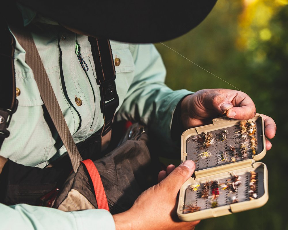 A man holds a fly fishing box filled with various flies, preparing for fly fishing in Aspen