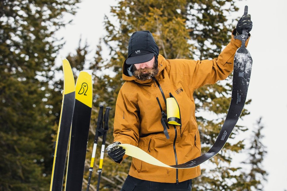 A man in a yellow jacket holds a pair of skis, preparing for adventure at Highland Bowl Aspen.