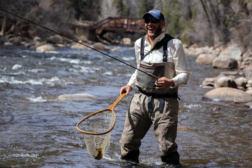 A man holds a fishing net in the river, with his captured fish in Aspen