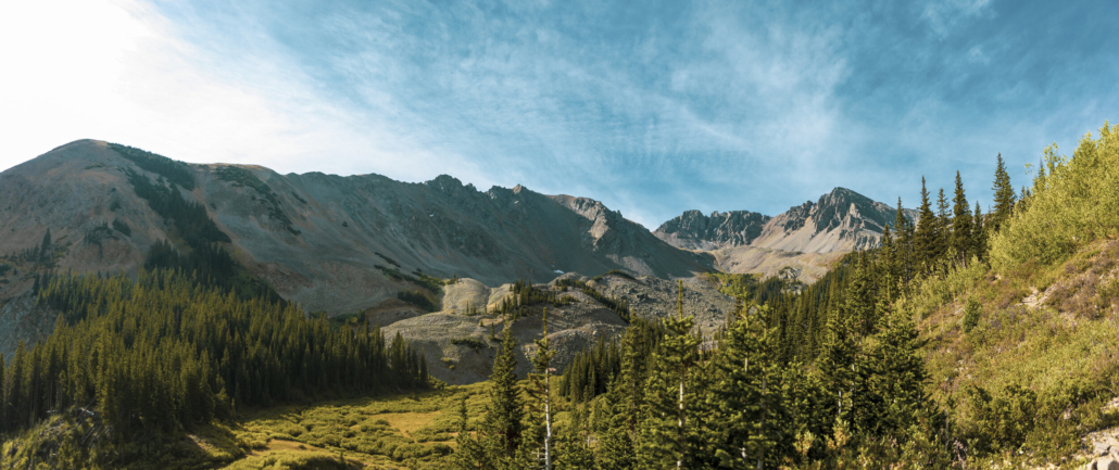 Aspen Guides - Majestic mountains rise above a landscape of green trees and grass, showcasing nature's beauty.