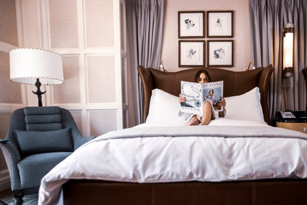 A woman reading a newspaper on a hotel bed with luxury interior room design