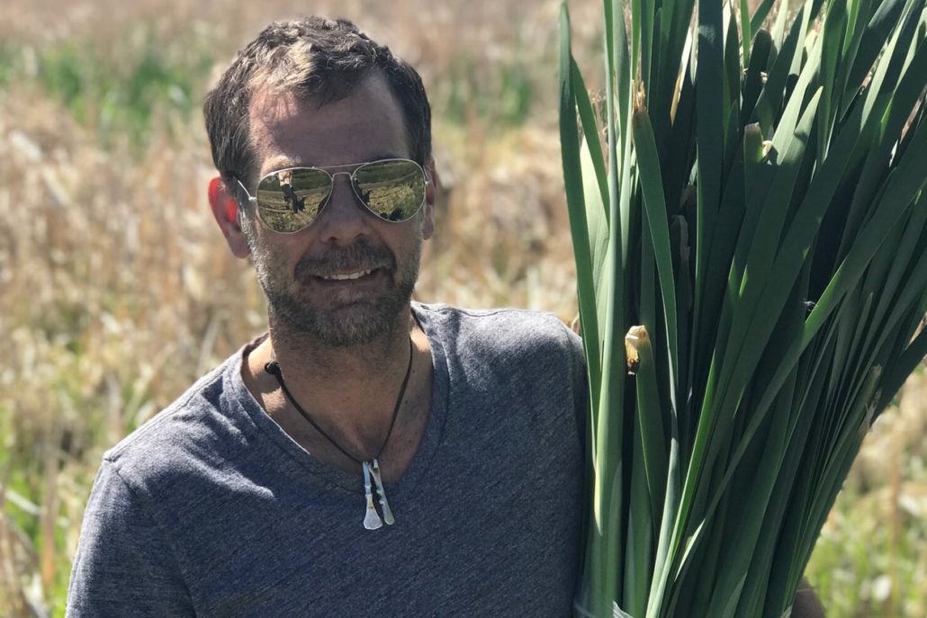 Chef Dodge wearing sunglasses holds a fresh bunch of green leaves, ready for culinary use.