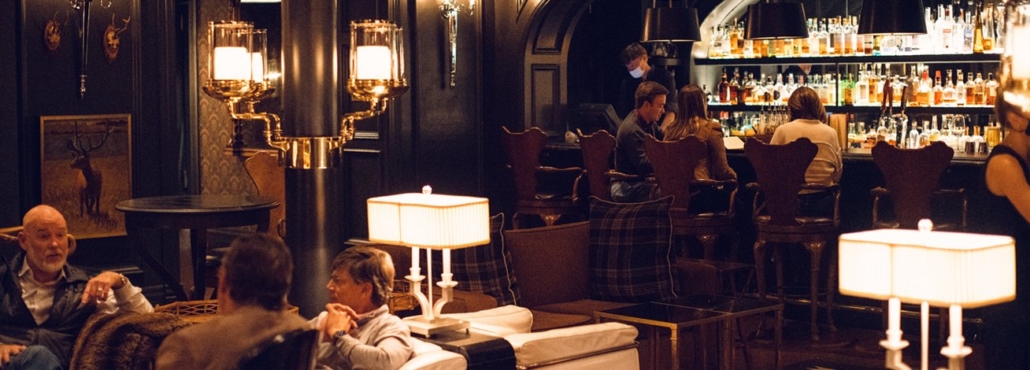 People seated at tables in a bustling bar, engaging in conversation and enjoying their drinks.