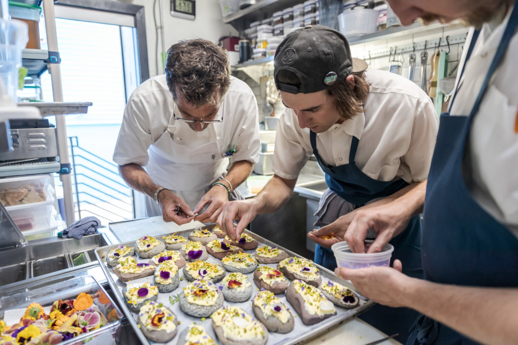 Three chefs are engaged in food preparation, showcasing teamwork in a professional kitchen setting.