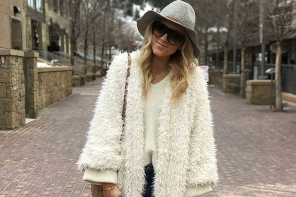 Blonde woman wearing a white fuzzy coat and hat, embodying Aspen Style in a snowy environment.