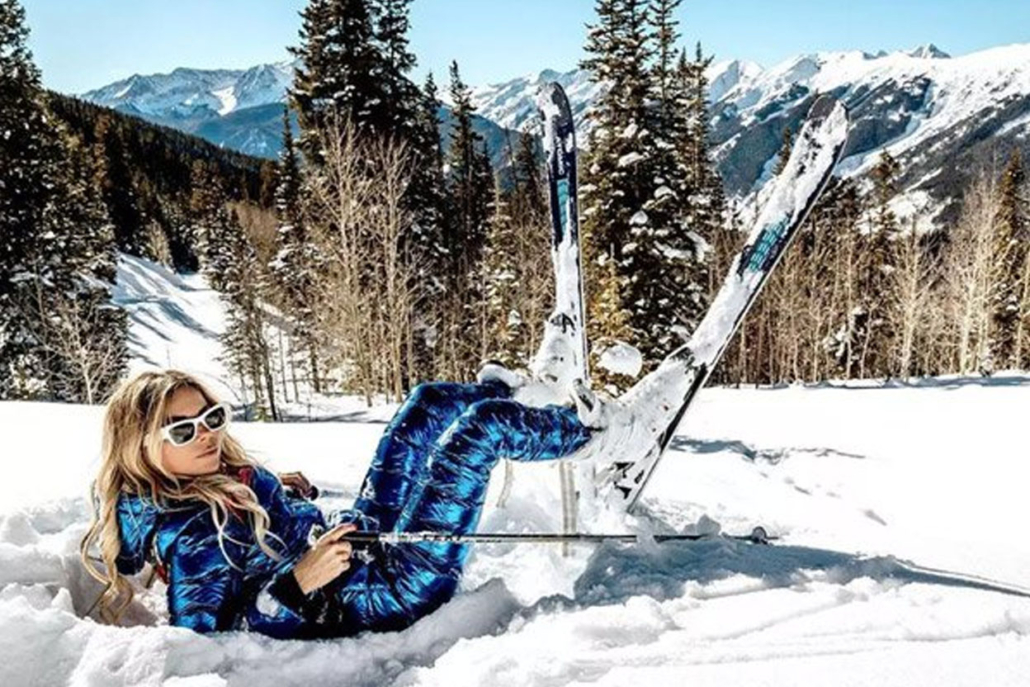 A woman dressed in blue ski attire lies on the snow enjoying the spirit of winter in Aspen.