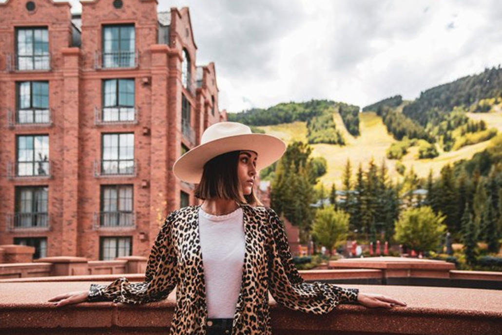 A woman in a stylish hat and clothes poses confidently, showcasing her unique fashion sense.