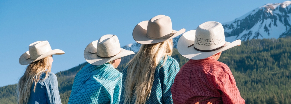 A group of people wearing cowboy hats, representing Aspen Hats, stand against a mountain, enjoying the outdoor scenery.
