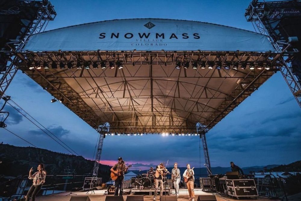 A vibrant scene from the Snowmass Music Festival, showcasing musicians performing outdoors amidst a festive crowd.