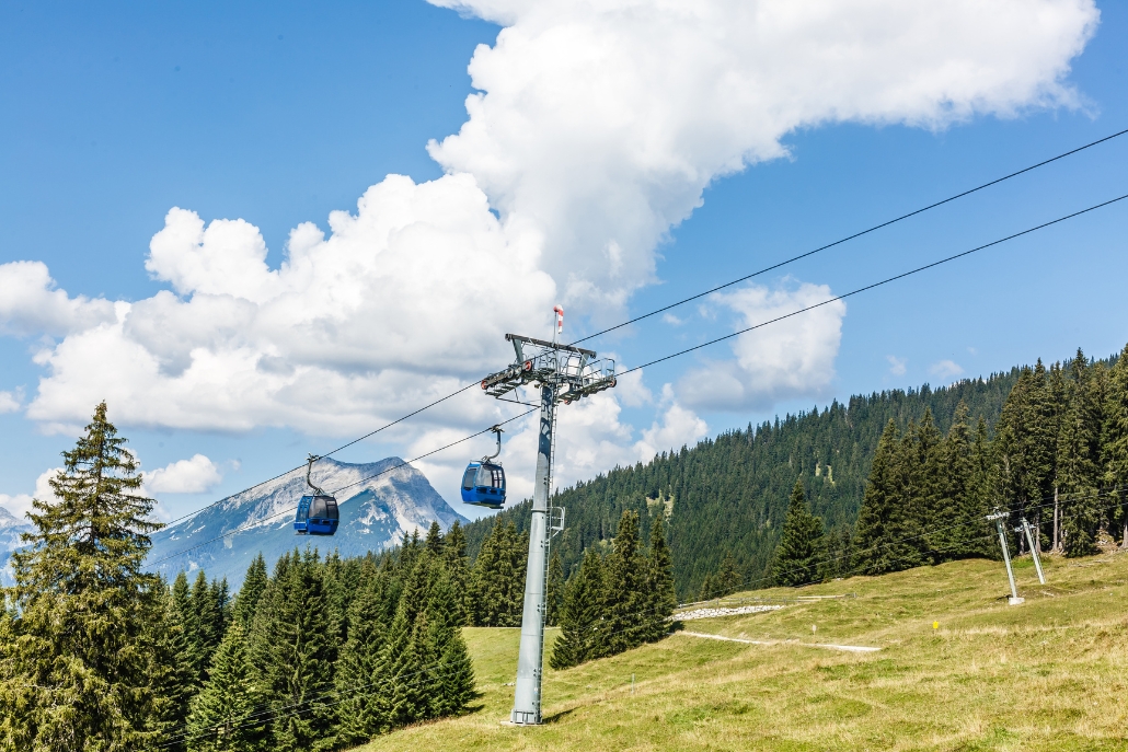 A scenic view of the Elk Camp Gondola ski lift in Snowmass Village, Colorado, framed by trees and cloudy skies.