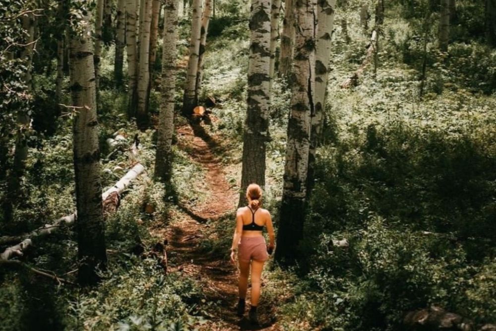 A woman hiking in a tranquil forest, enjoying nature's beauty and peace in Snowmass Village Colorado