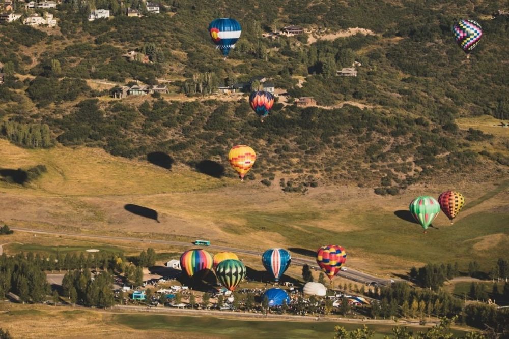 A vibrant scene of numerous hot air balloons soaring above a picturesque hillside landscape.