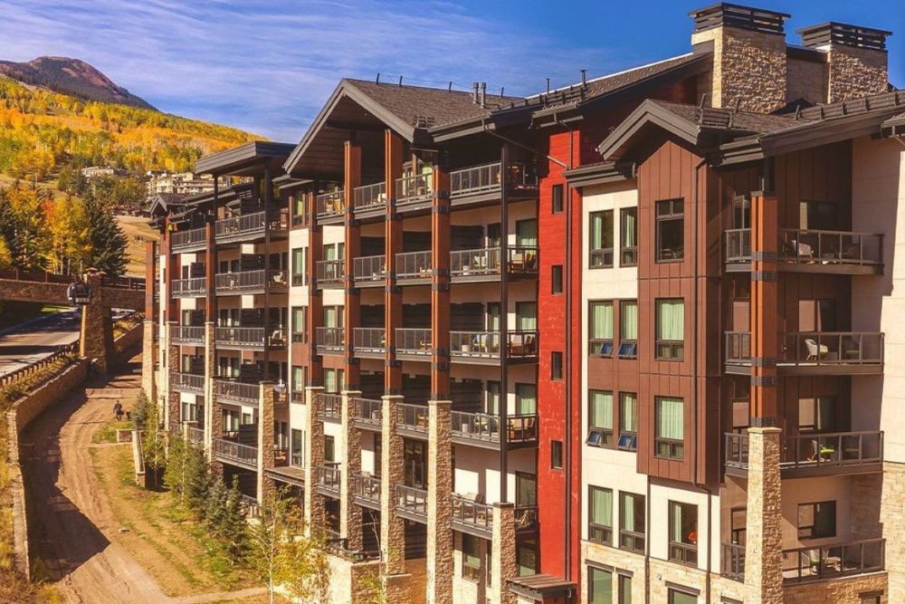 A large apartment building with balconies, set against a backdrop of majestic mountains in Snowmass Village Colorado