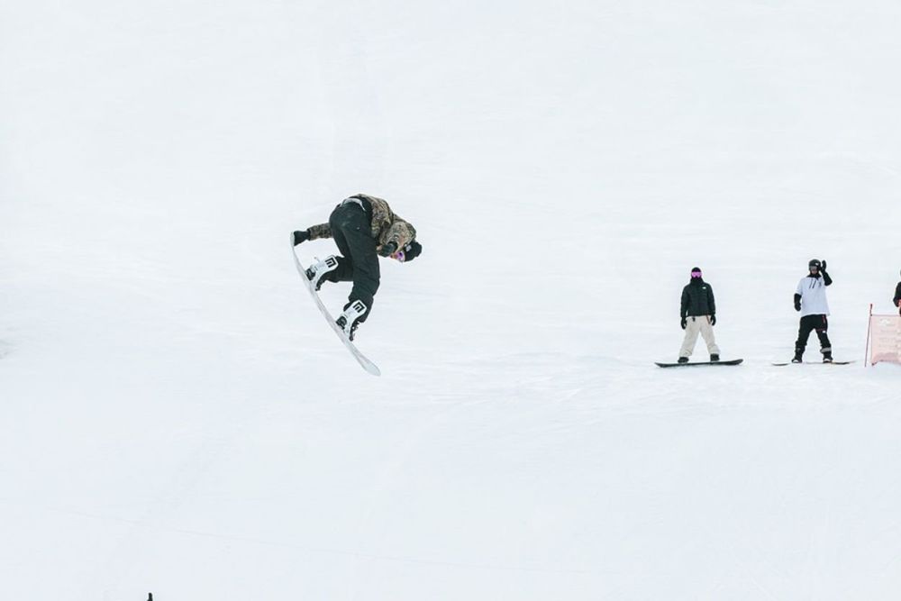 A snowboarder performs an impressive aerial trick against a snowy backdrop in Snowmass Village Colorado.