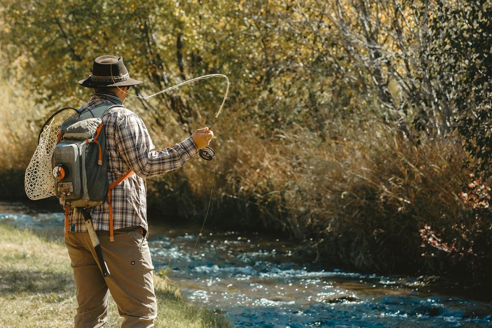 Angler fly fishing in a serene river surrounded by lush foliage in Aspen