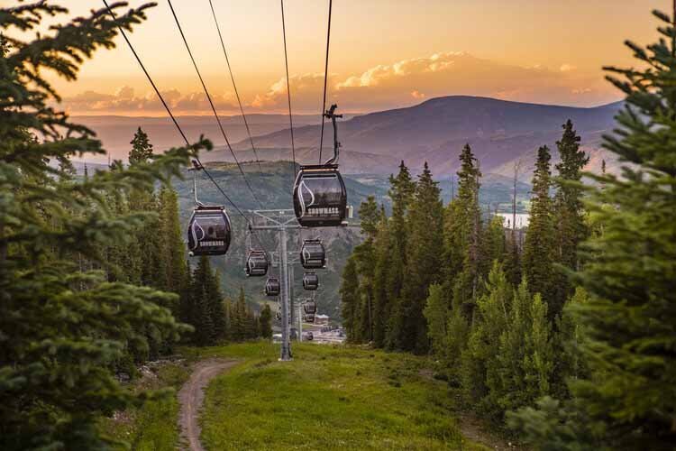 Sunset view of a gondola ride over a green mountainous landscape in Aspen in July