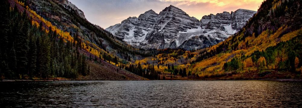 The majestic Maroon Bells rise above a tranquil lake, framed by colorful fall trees.