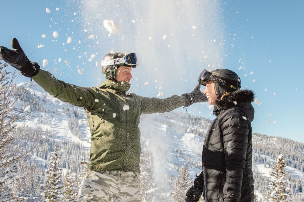 Two individuals stand in a snowy landscape, surrounded by falling snowflakes, enjoying the winter scene.