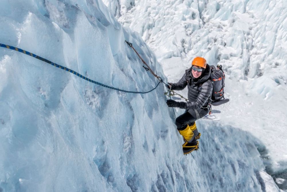 A climber wearing an orange jacket and helmet scales a large ice wall, demonstrating winter adventure activities.