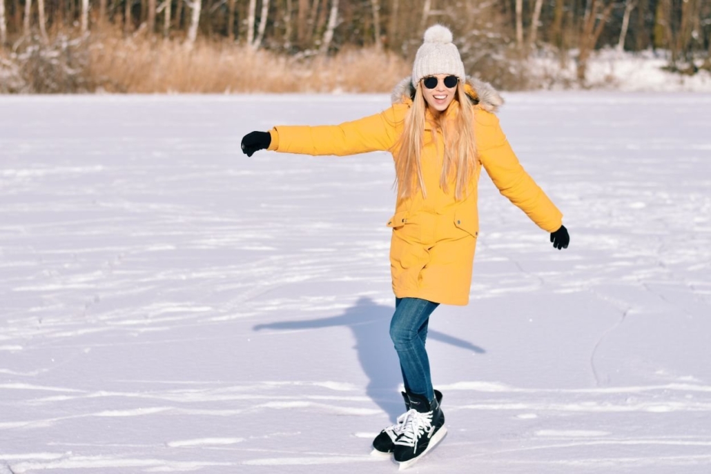 A woman in a yellow coat and sunglasses gracefully skates on a frozen lake, enjoying one of the things to do in Aspen in Winter.