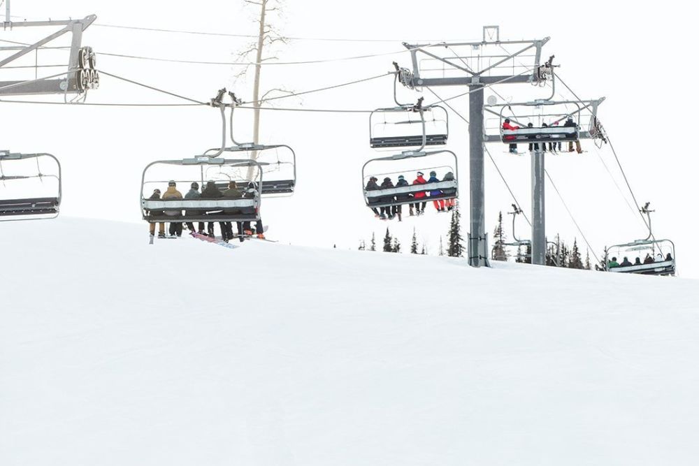 People enjoying a ski lift ride, ascending a winter landscape with a chair lift in the background.