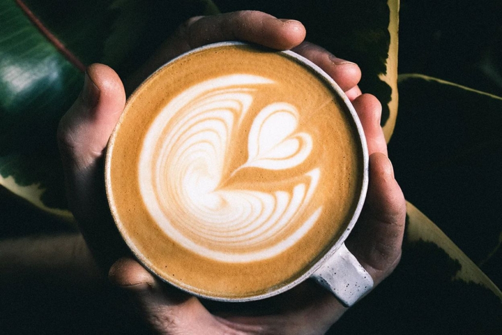 A person holds cup of coffee adorned with a heart design, showcasing the cozy atmosphere of Felix Coffee Roasting Co.